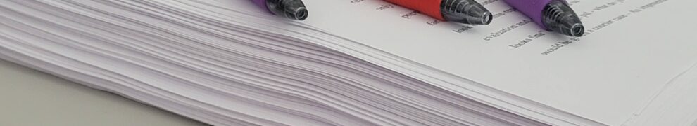 A stack of paper representing a finished novel with pens nearby for editing