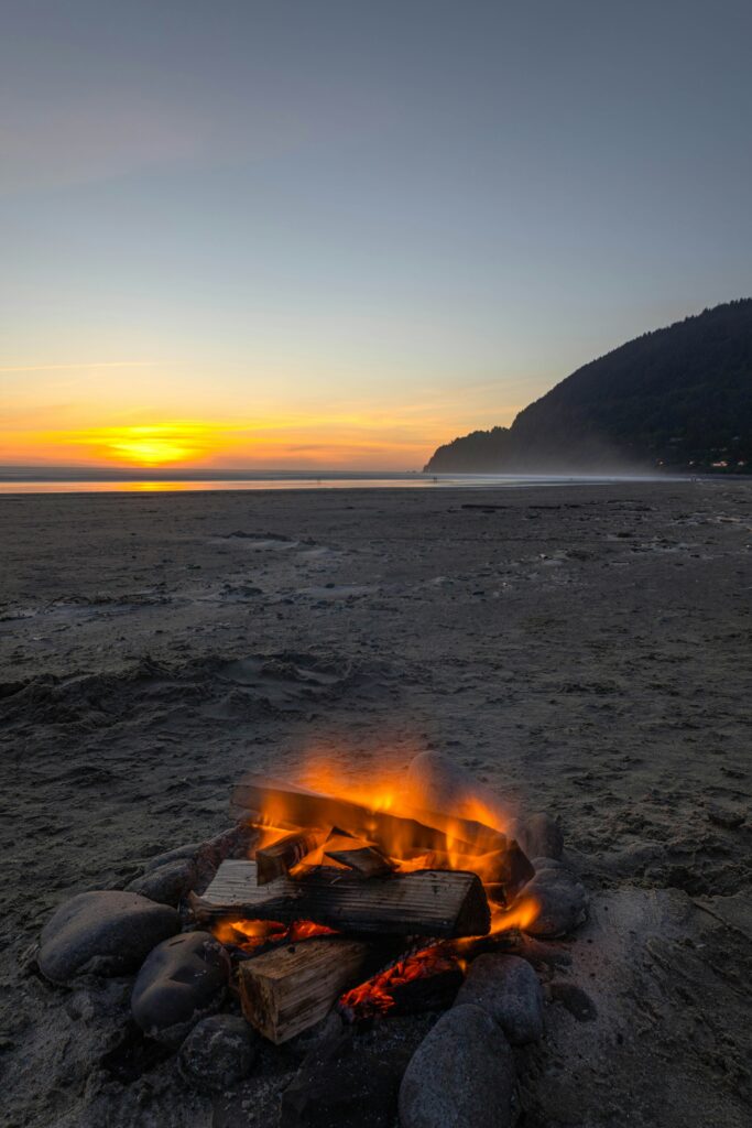 A small fireplace burning on the beach near the ocean during sunset.